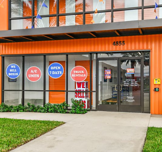 Value Store It facility exterior with blue circular signage advertising sell boxes, A/C units, open daily, and truck rental.