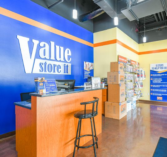 Value Store It office interior with blue and orange branding, reception desk, and informational signage.