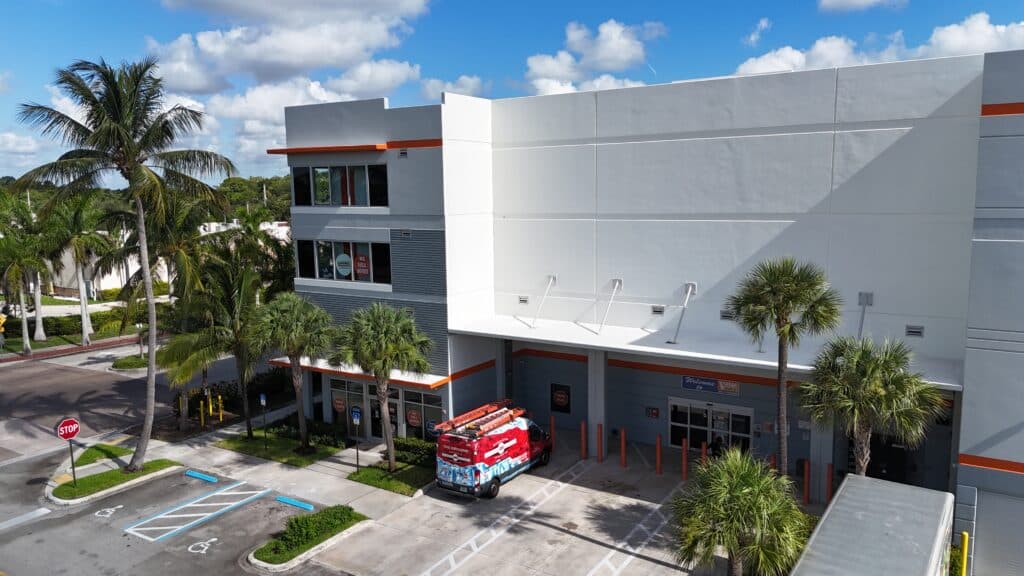 Modern self-storage facility exterior with red and white branding, palm trees, and emergency vehicle parked in front.